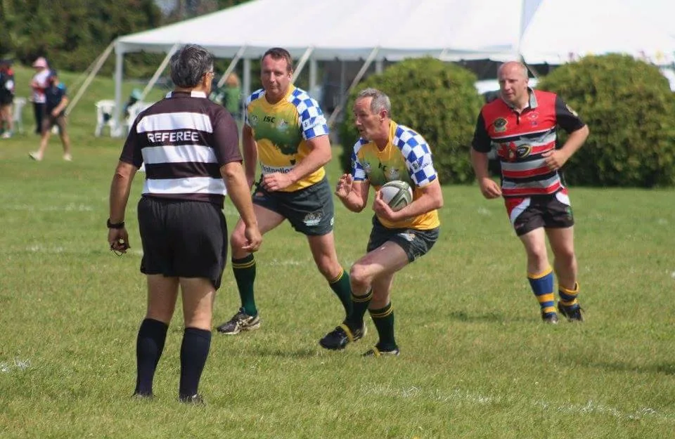 Golden Oldies rugby players and a referee during a match on a grass field