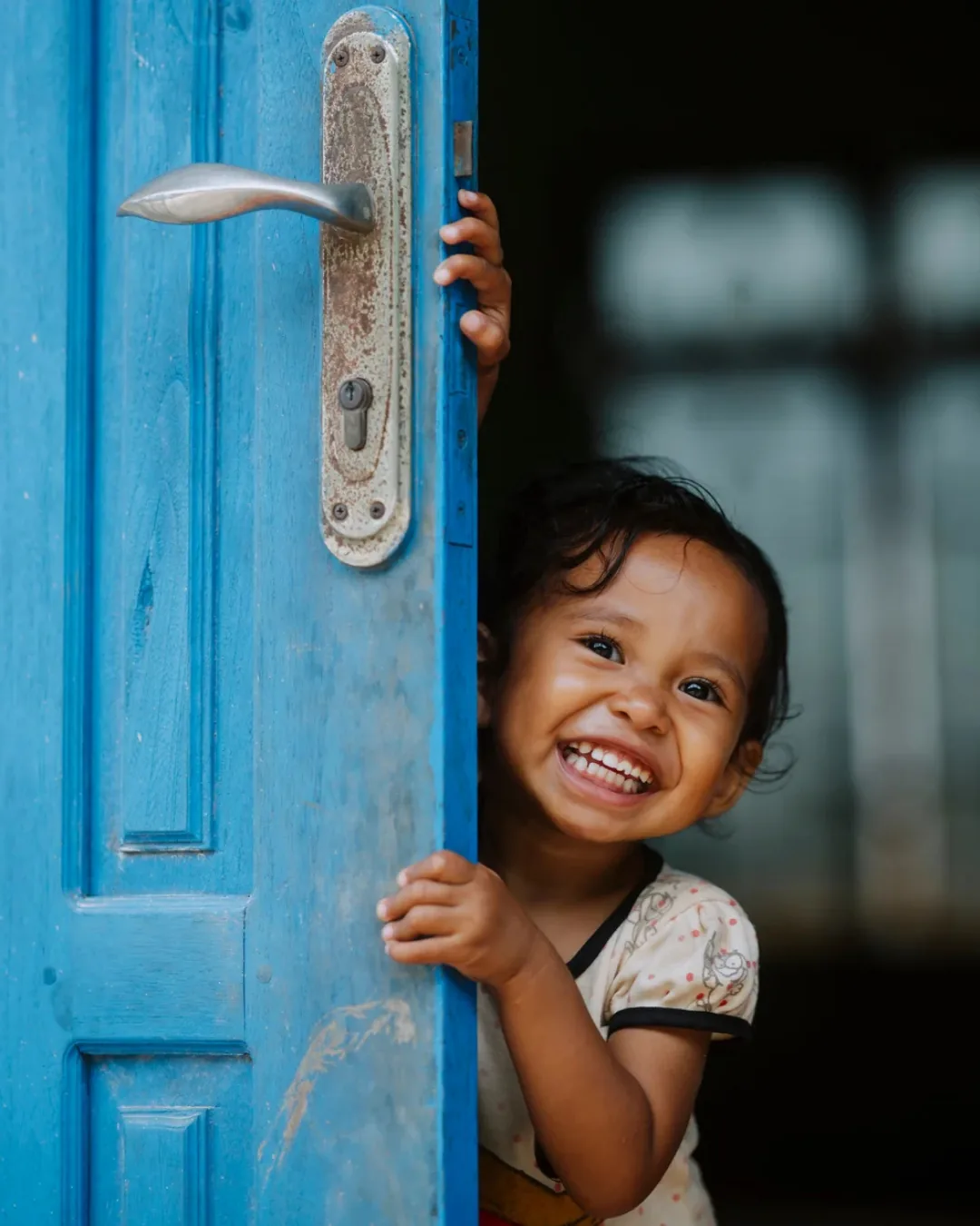 A smiling young child leaning around a bright blue wooden door