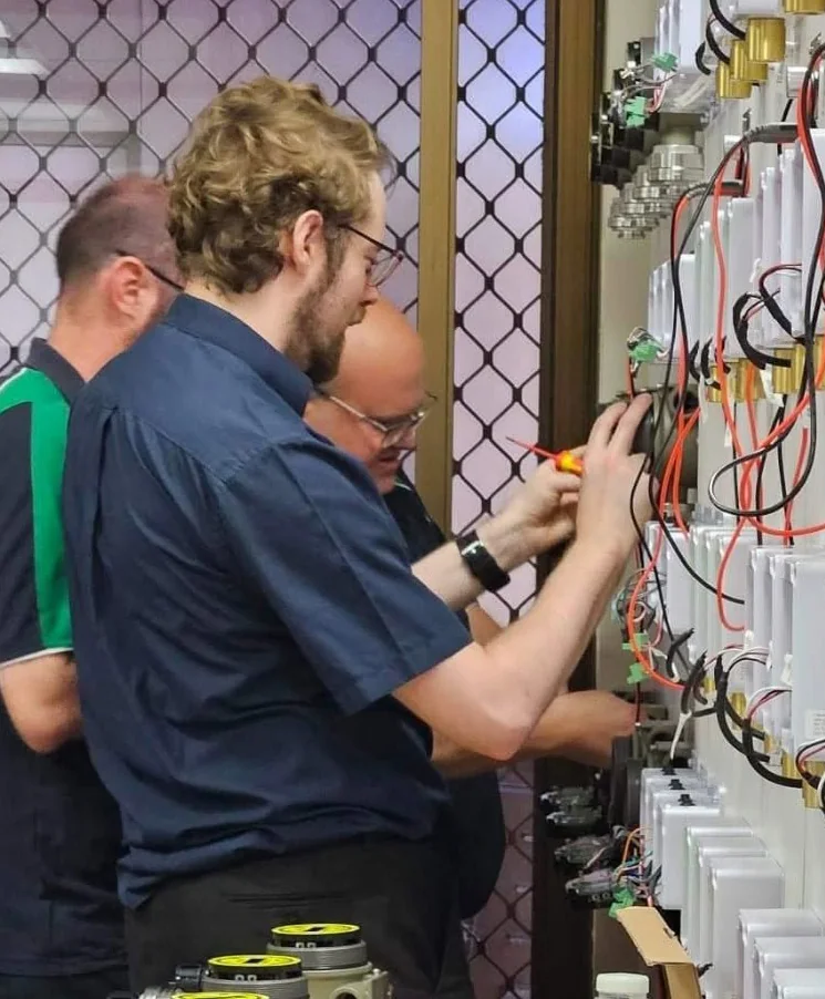 Two Gas Detection Australia technicians wiring and testing gas detectors on the workshop panel wall