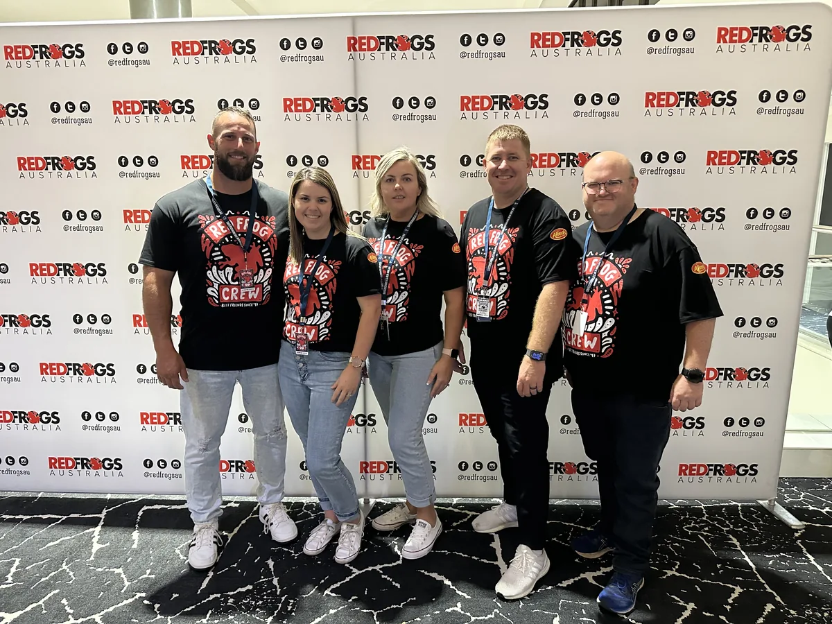 Five Red Frogs Australia crew members in branded shirts in front of a Red Frogs backdrop