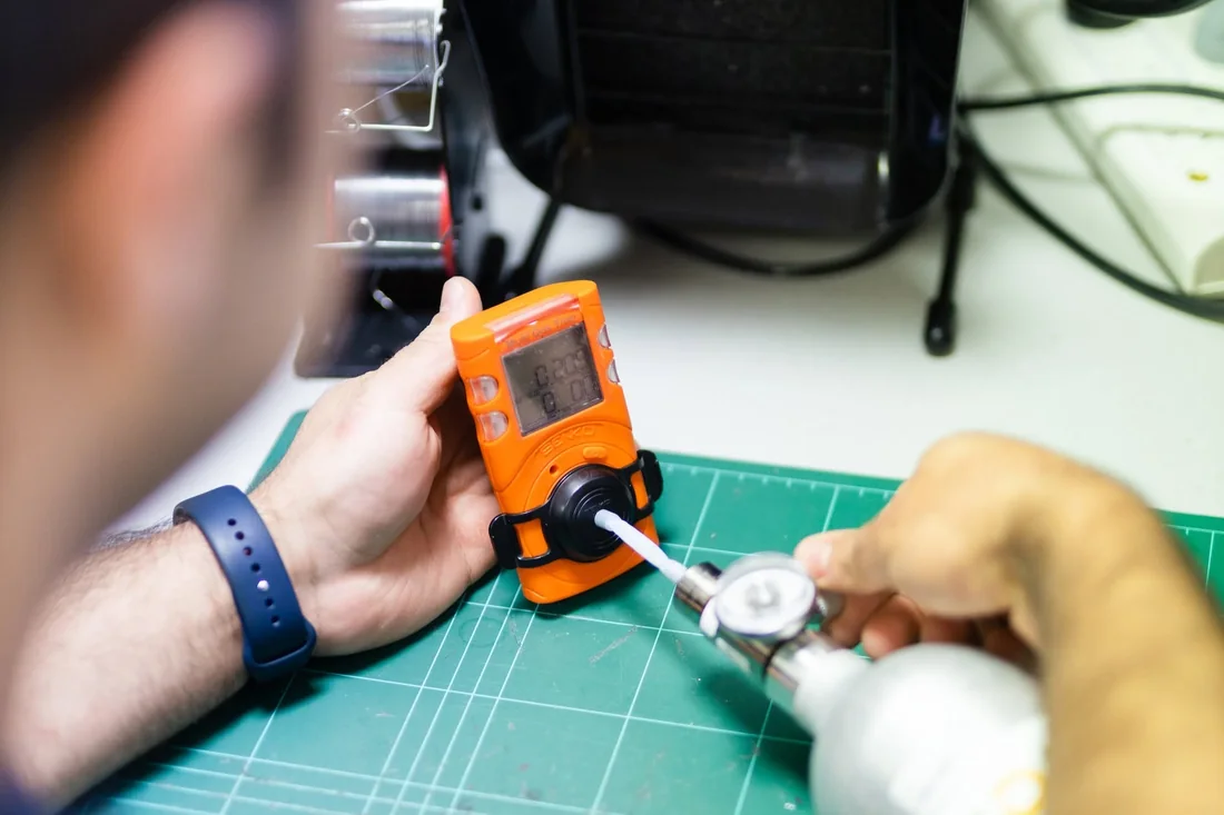 A Gas Detection Australia technician bump testing an orange portable gas detector with calibration gas